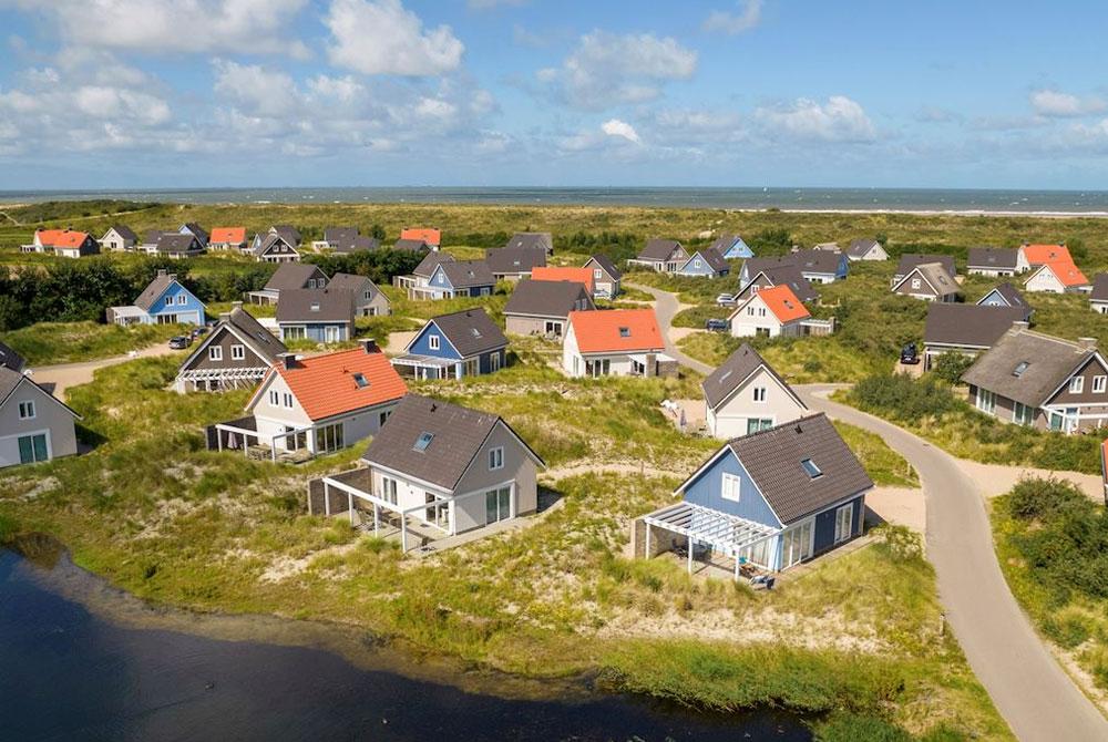 Luchtfoto van een vakantiepark met kleurrijke huisjes in de duinen, dicht bij zee